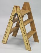 A NOVELTY PAIR OF CREAM FOLDING WOODEN STEPS