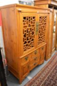 A Chinese soft wood cabinet with lattice work doors enclosing shelves and two drawers above an