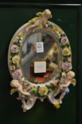 A Dresden porcelain and cherub encrusted mirror.