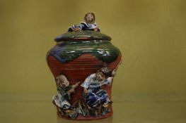 A pottery jar and cover decorated with moulded figures of children.