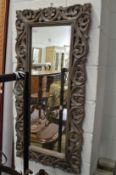 A wall mirror with decoratively carved frame.