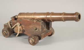 A GOOD SMALL BRONZE CANNON on a wooden carriage with four wooden wheels.