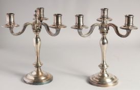 A PAIR OF CHRISTOFLE SILVER PLATED THREE BRANCH CANDELABRAS ON circular loaded bases. 10ins high.