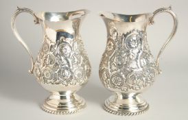 A GOOD PAIR OF CONTINENTAL SILVER PLATED WATER JUGS with floral repousse decoration. 9.5ins high.