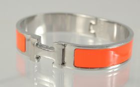 A HERMES ORANGE AND CHROME BANGLE.