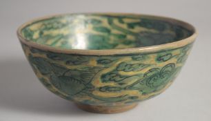A GREEN GLAZED POTTERY BOWL, painted with cranes in flight and stylised clouds, 17.5cm diameter.
