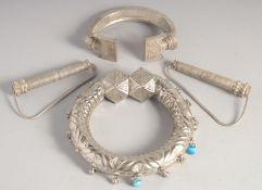 TWO EASTERN EMBOSSED WHITE METAL LARGE BANGLES and a pair of white metal clasps, combined weight