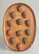 A GOOD COLLECTION OF JAPANESE TERRACOTTA MINIATURE NOH MASKS mounted to an oval wooden plaque, the