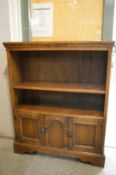 A small oak open bookcase with cupboards below.