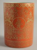 A CHINESE CORAL RED PORCELAIN BRUSH POT, with gilt floral decoration and characters to the exterior,