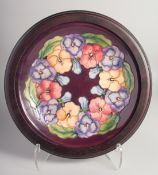 MOORCROFT PANSY DESIGN PLATE in an oak frame. 9.5ins diameter