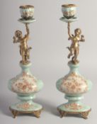 A PAIR OF BRONZE AND PORCELAIN CHERUB CANDLESTICKS. 14ins high.