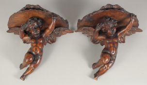A PAIR OF CARVED WOOD CUPID WALL BRANCHES. 17ins long.