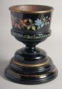 A VICTORIAN BLACK URN painted with flowers on a wooden stand. 8ins high
