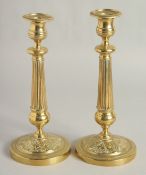 A PAIR OF EMPIRE ORNATE CANDLESTICKS on circular bases. 11ins high.
