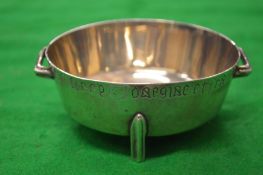 A small circular silver twin handled bowl on three peg feet, the rim with engraved inscription.