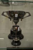 A large silver plated twin handled trophy cup on stand and a small trophy cup.