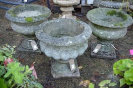 Three composite garden urn shaped planters on square bases.