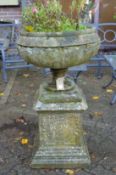 A large composite circular garden planter on an ornate pedestal base.