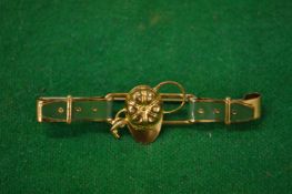 A decorative bar brooch modelled as a belt with jockey cap and whip.