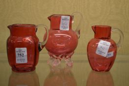 Three small cranberry glass jugs.