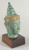 A THAI METAL BUDDHA HEAD, with gilded headpiece and mounted to a wooden base, head 22cm high.