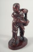 A CARVED HARDWOOD FIGURE OF A BOY carrying a satchel upon an oval shape base, possibly Republican,