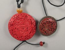 A RED CIRCULAR PENDANT carved with a dragon, and a CINNABAR LACQUER FLORAL BROOCH with filigree
