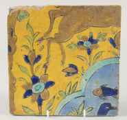 AN 18TH CENTURY PERSIAN SAFAVID YELLOW GLAZED TILE, painted with fish and flora, 23cm square.