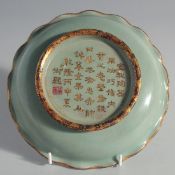 A CHINESE CELADON PETAL FORM DISH, with gilt rim and gilt characters to the base, 19.5cm diameter.