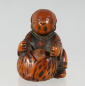 A JAPANESE CARVED WOODEN NETSUKE of a seated figure, with a fruit in his lap, with moving inset