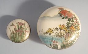 TWO JAPANESE SATSUMA CIRCULAR BOXES, the larger painted with flora over water with mountains beyond,