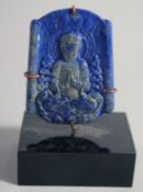 A CHINESE CARVED LAPIS LAZULI BUDDHISTIC PENDANT, on stand, the pendant measuring 5cm x 4cm.