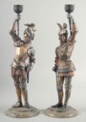A PAIR OF PAINTED AND GILDED CANDLESTICKS men in suits of armour on circular bases. 16ins high.