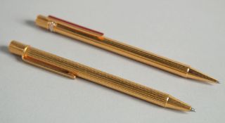 TWO CARTIER GILT PENS in a red pouch.