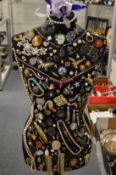 An unusual dressmaker's mannequin on stand decorated with numerous bijouterie items to include