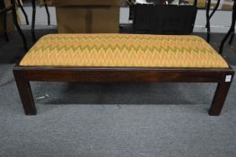 A long footstool with upholstered top on square legs.