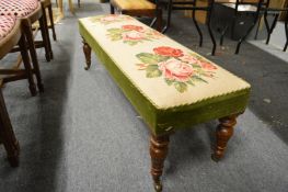 A floral embroidered long footstool on turned legs with brass castors.