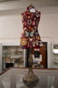 A miniature dress makers mannequin decorated with numerous brooches, pendants etc.