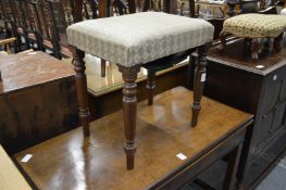 An upholstered mahogany framed stool on turned legs.