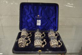 A cased set of six glass tots with pierced silver holders (one glass missing).