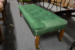 A button upholstered long footstool on tapering legs with brass castors.