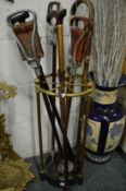 A brass and cast iron circular stick stand with various sticks and shooting sticks etc.
