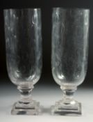 A SMALL PAIR OF GLASS STORM - HURRICANE LAMPS on square bases. 13ins high.