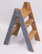 A PAIR OF NOVELTY CHAMPAGNE WOODEN FOLDING STEPS. 30ins high.