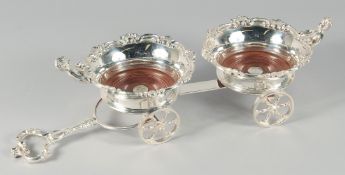A GOOD SILVER PLATE DOUBLE TABLE COASTERS with cupids on two pairs of wheels. 17ins.