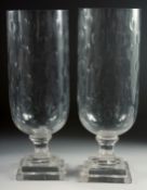 A LARGE PAIR OF GLASS STORM - HURRICANE LAMPS on square bases. 16ins high.