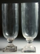 A SMALL PAIR OF GLASS STORM - HURRICANE LAMPS on square bases. 13ins high.