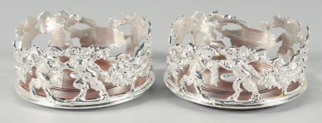 A PAIR OF SILVER PLATED CHERUB CIRCULAR WINE COASTERS with turned wood bases. 5ins diameter.