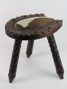 A carved wooden stool in the form of a horse shoe having cow hide seat.